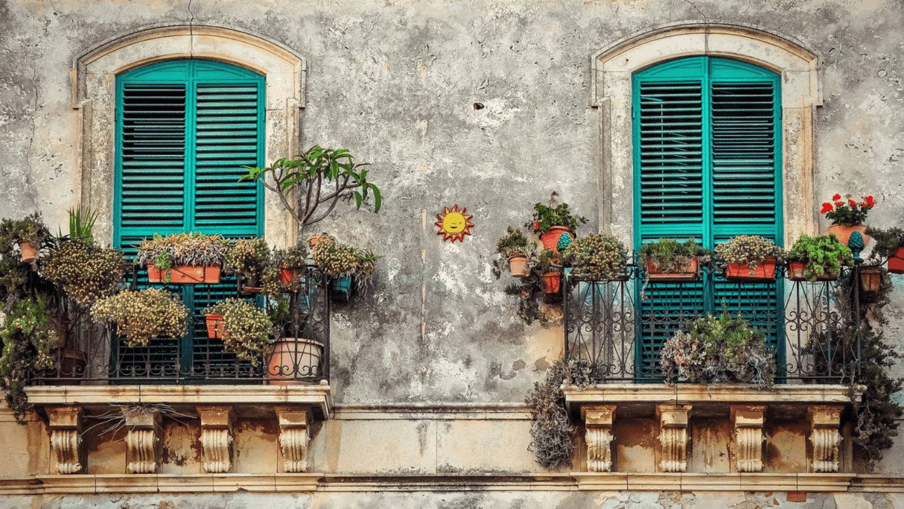 Historische italienische Hausfassade mit grünen Fensterläden und bepflanzten Balkonen